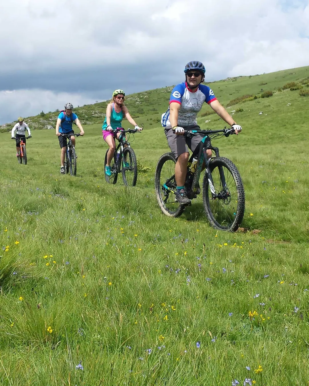 Grupa rowerzystów na singletracku przez zieloną łąkę