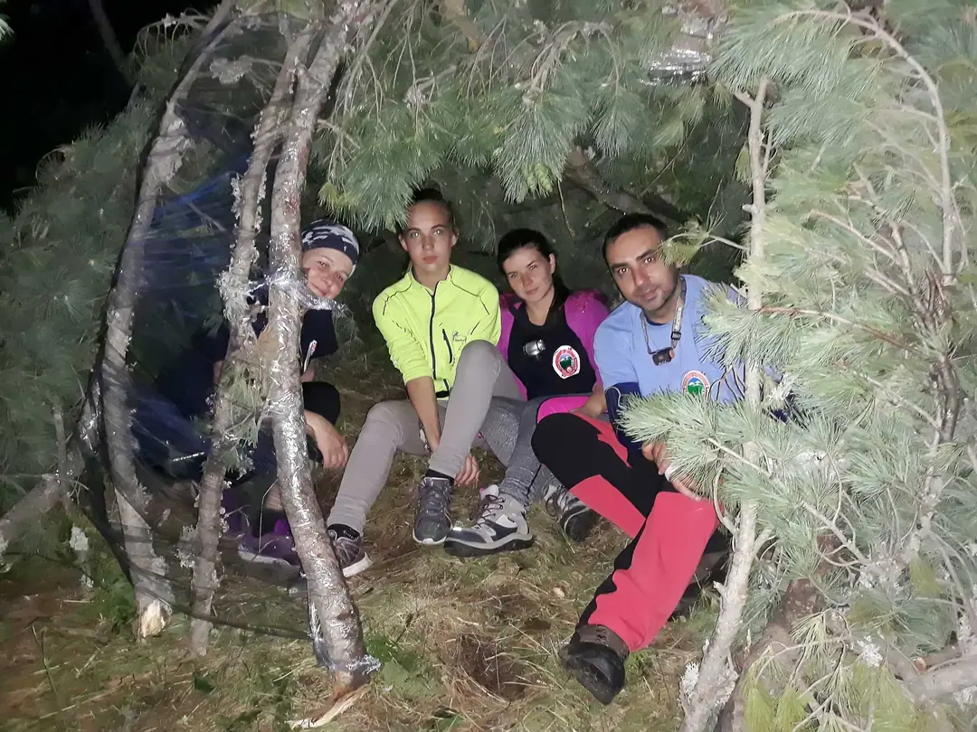 Team sitting in a shelter they built from branches