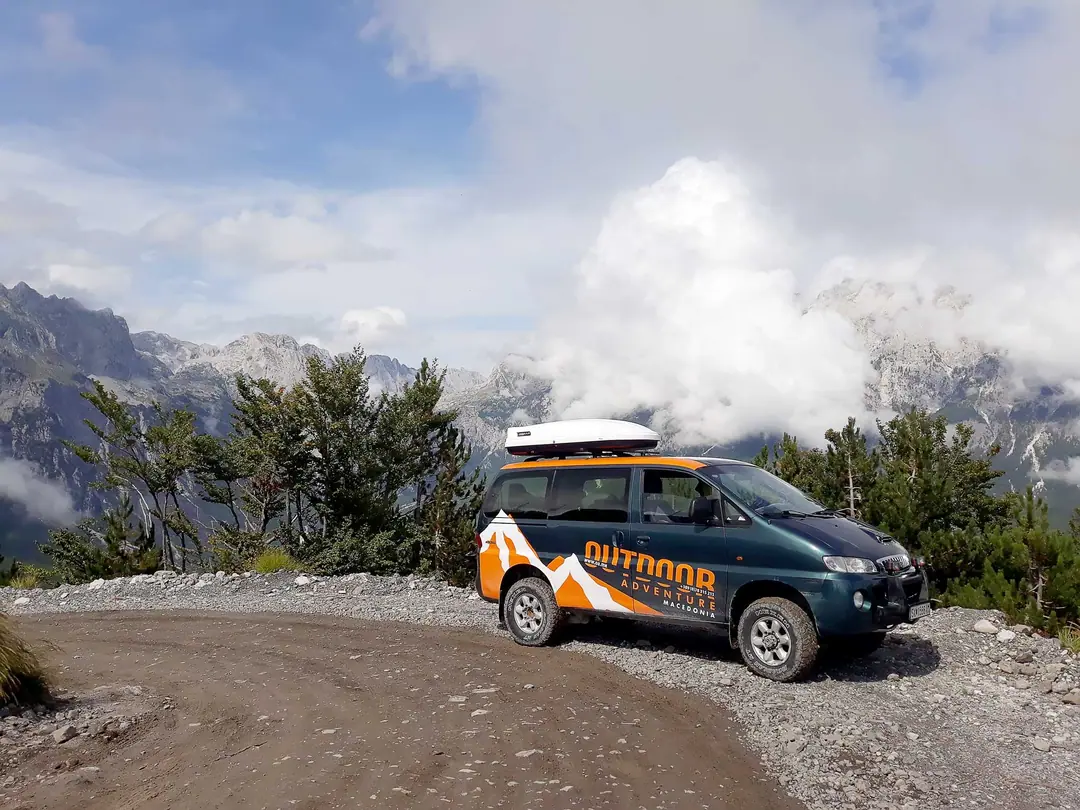 The 4x4 van on a gravel road with rocky peaks behind